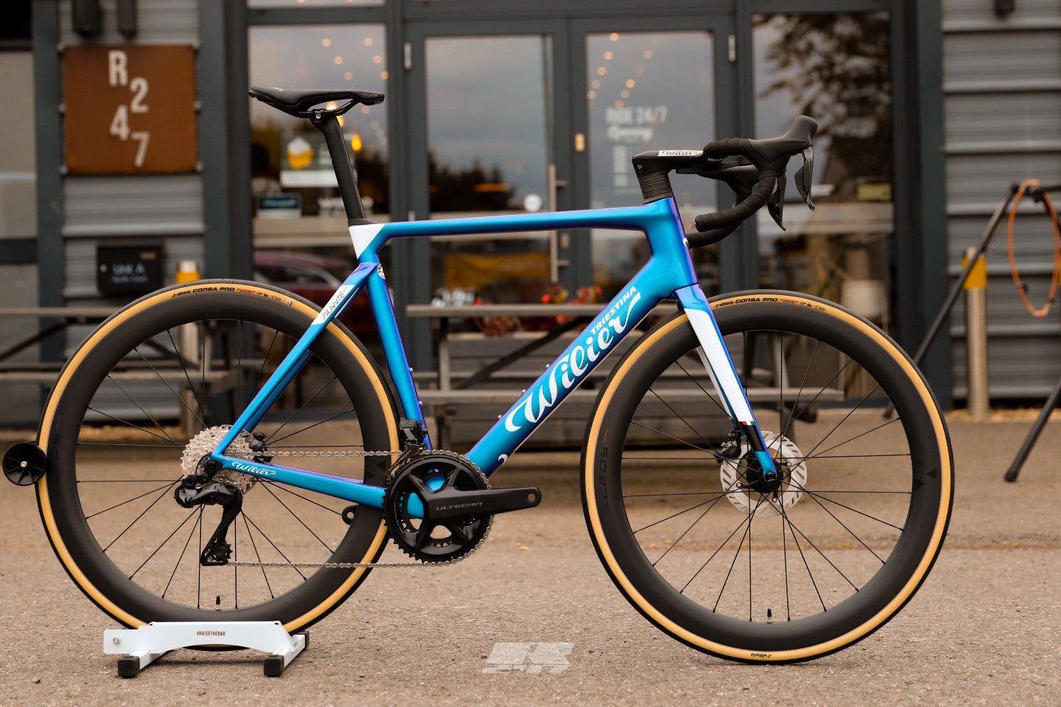 Blue bicycle on a stand in front of a building with large windows.