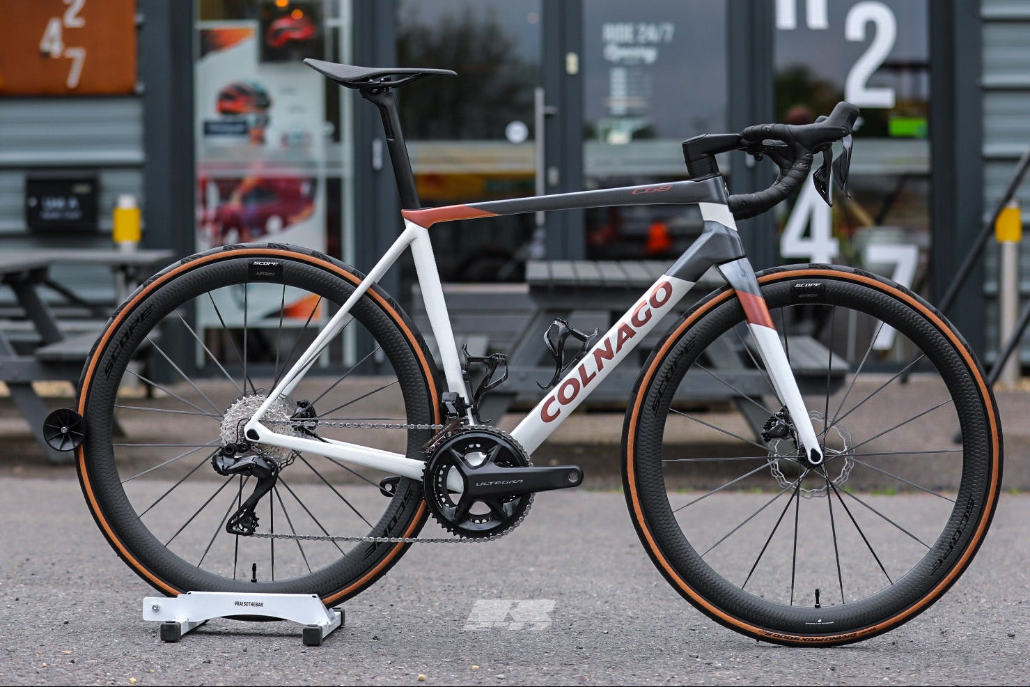 Colnago bicycle on a stand in front of a building with large windows.